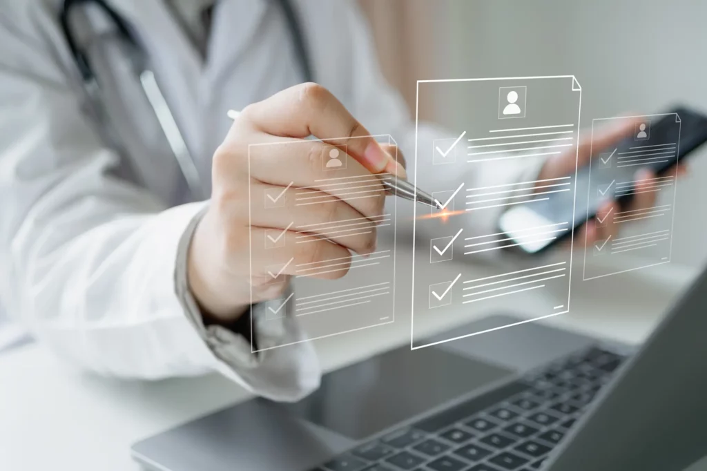 A person in a lab coat interacts with a floating digital checklist using a pen while holding a smartphone in the other hand. A laptop sits on the table suggesting a blend of technology and healthcare.